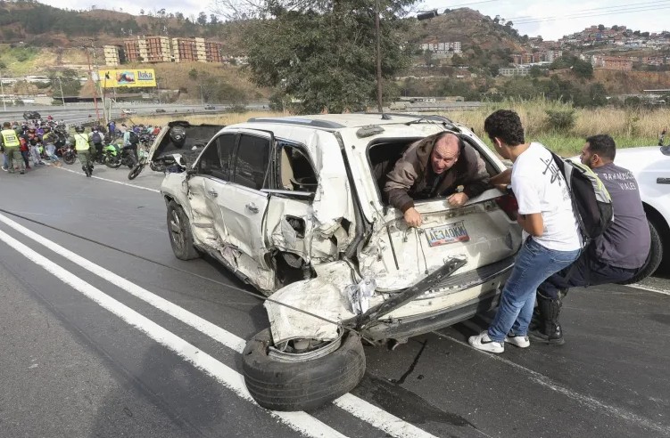 Varias personas ayudan a una persona a salir de un automóvil accidentado después de una colisión en una carretera principal en Caracas el 12 de febrero de 2025